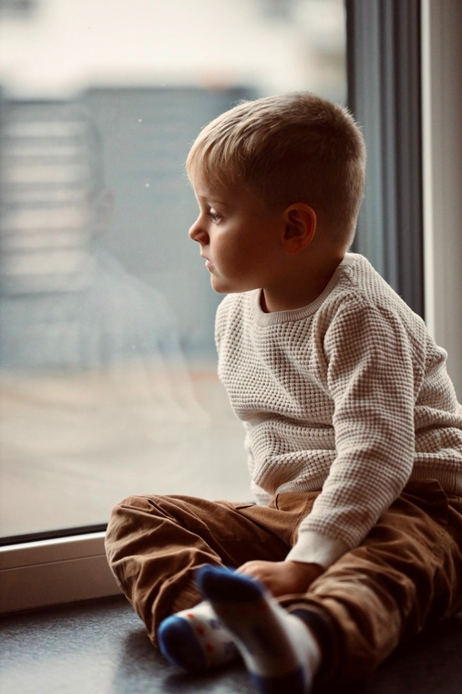Junge sitzt am Fenster und schaut hinaus